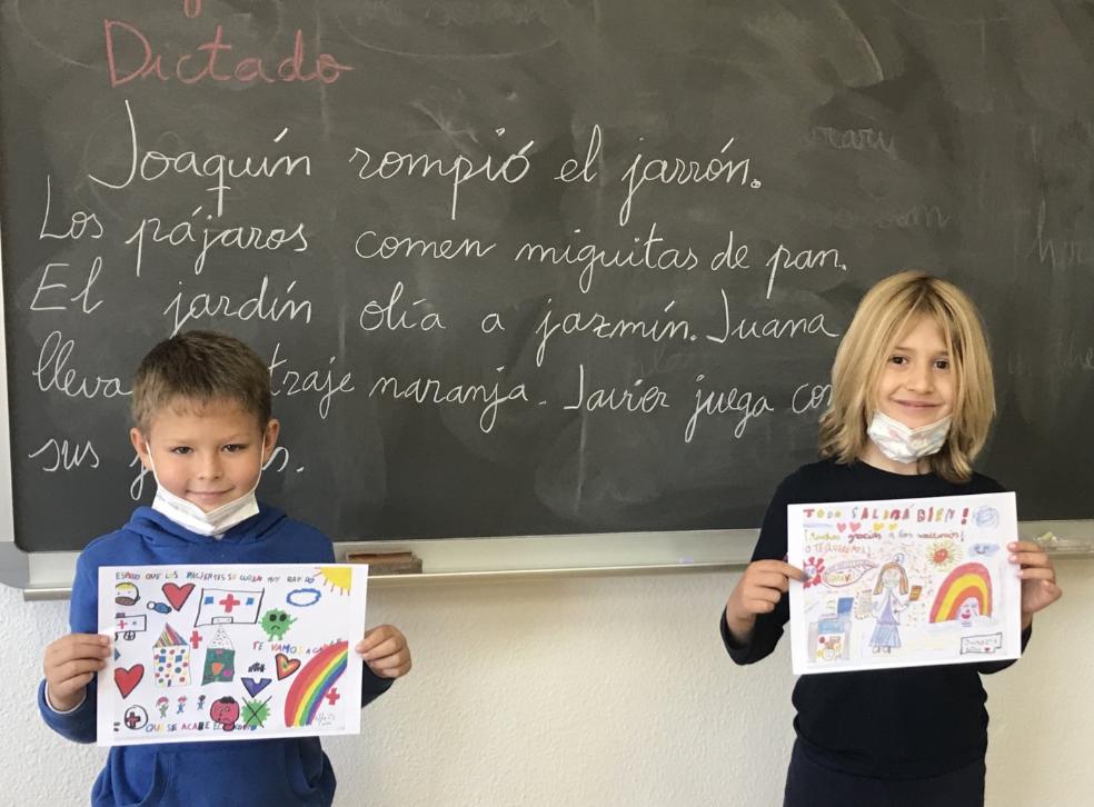 Dos alumnos del colegio San Fernando enseñan los dibujos que han mandado al hospital. / HOY