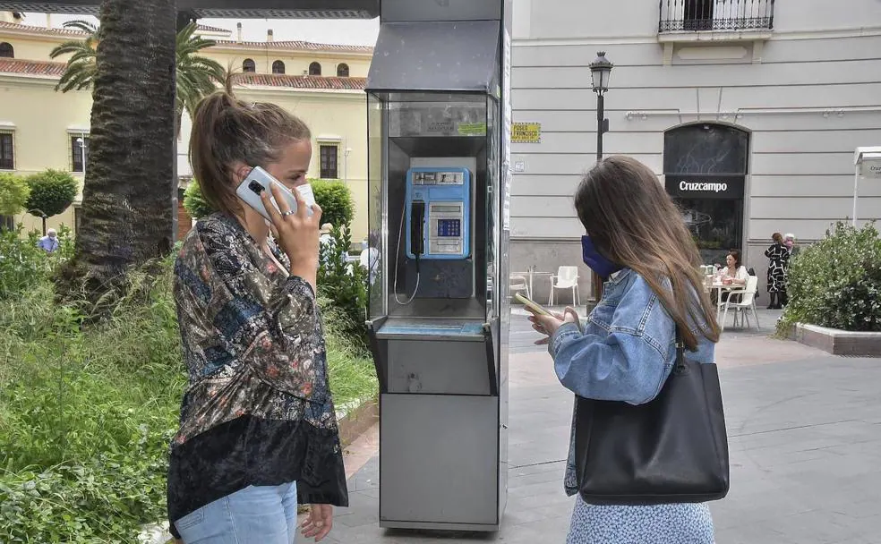 Dos jóvenes usan sus móviles junto a una cabina en Badajoz. /CASIMIRO MORENO